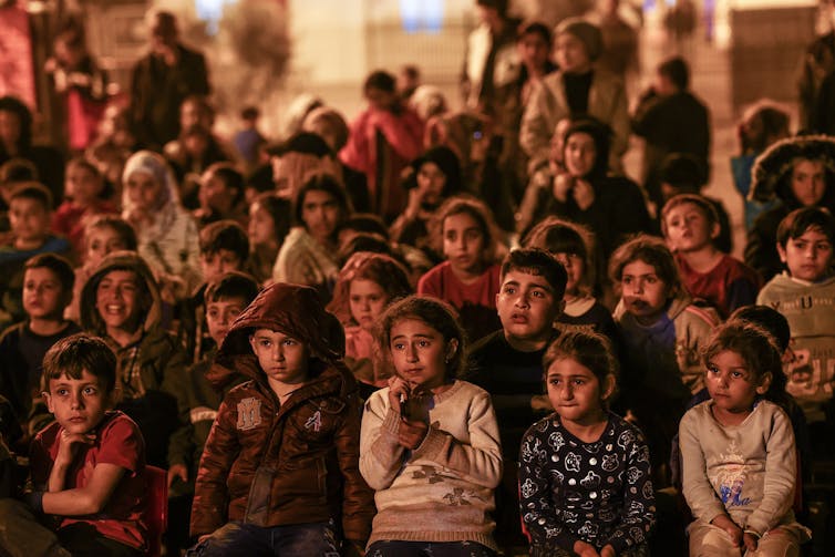 Young children watching a film inside a tent camp.
