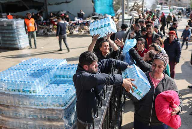 Aid workers distributing water bottles over a fence to a crowd of people.