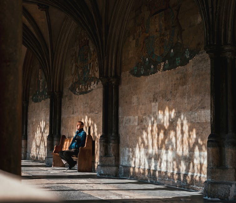 A person sits in a cloister with reflections on the wall.