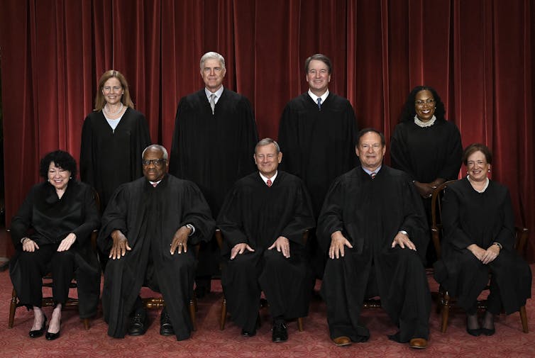 A group of nine people in black robes, seated in two rows.