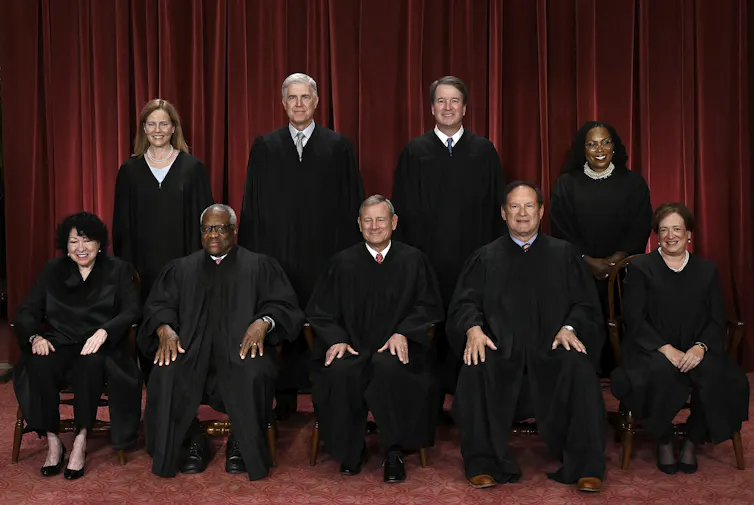 A group of nine people in black robes, seated in two rows.