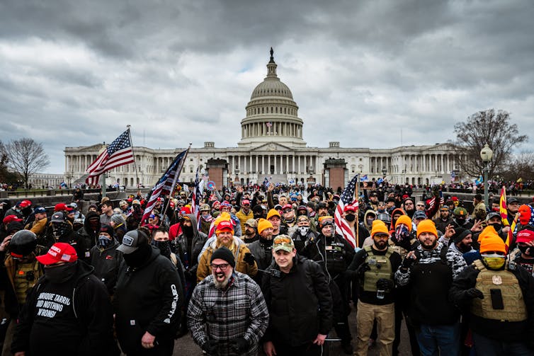 A large crowd of angry-looking people in front of the U.S. Capitol, a white-domed building.
