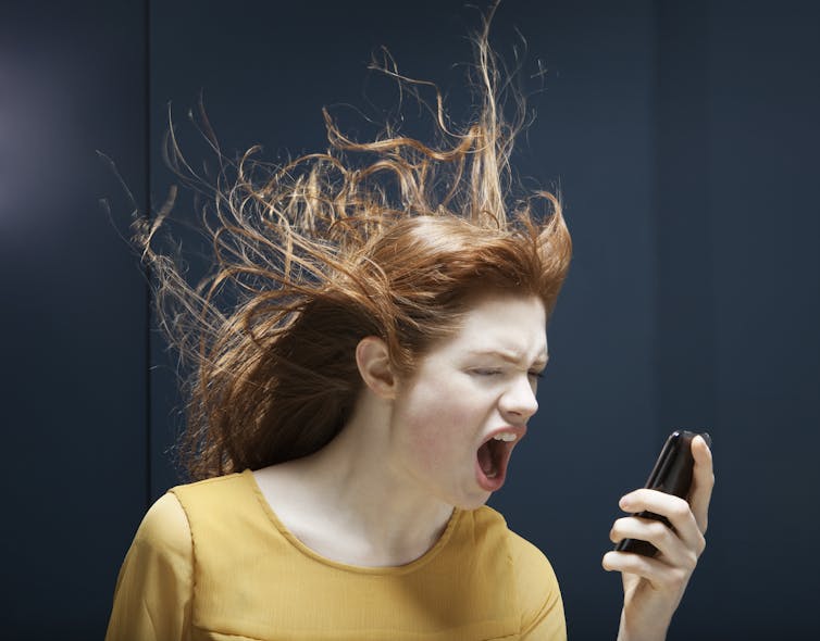 A woman yells into a phone with her hair blowing up and back