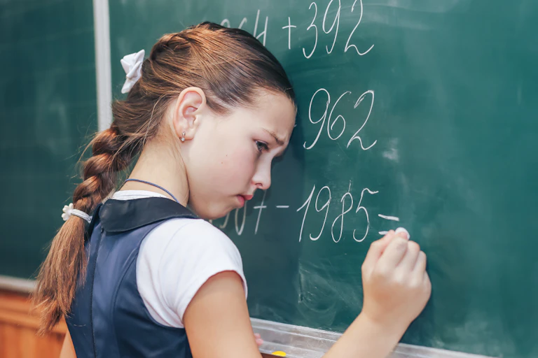 Une écolière en train de résoudre des opérations de maths au tableau