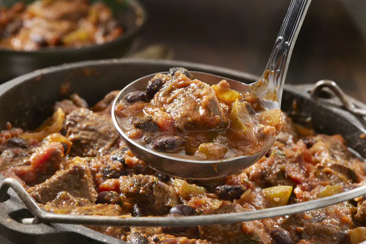 A ladle holds some chili above a simmering pot full of food.