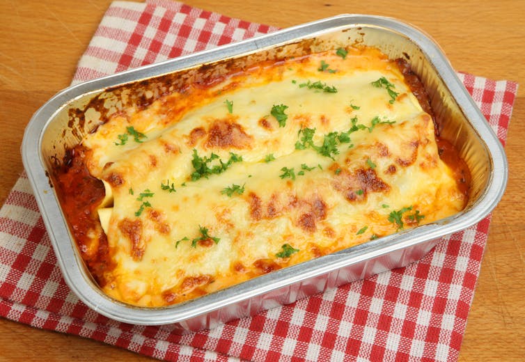A foil pan of a dish covered in cheese.
