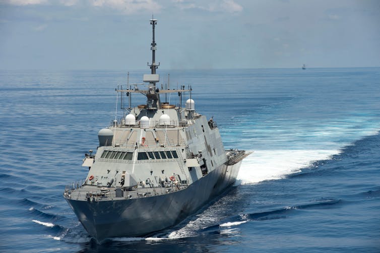 A US naval vessel sailing through a deep blue sea.