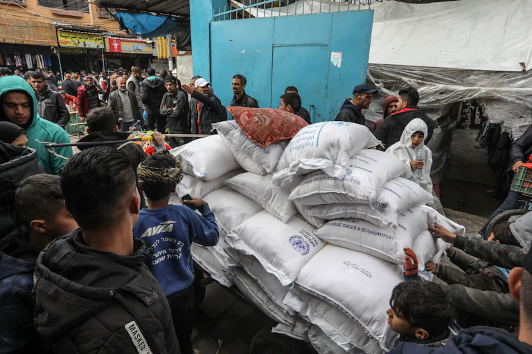 Personas en torno a un montón de sacos blancos de UNRWA.