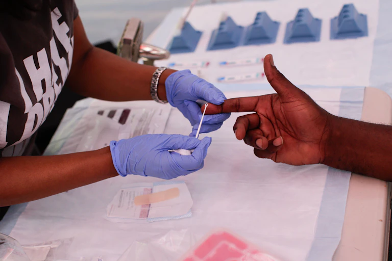 A person wearing gloves is holding a Black man's finger as they extract a sample of blood.