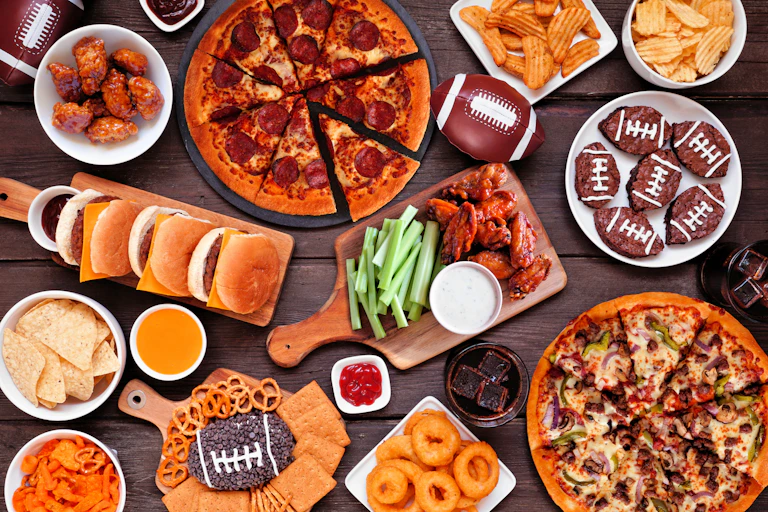 An overhead view of a table filled with all kinds of food, including pizza, chips and dip, cookies decorated like footballs, pretzels and onion rings.