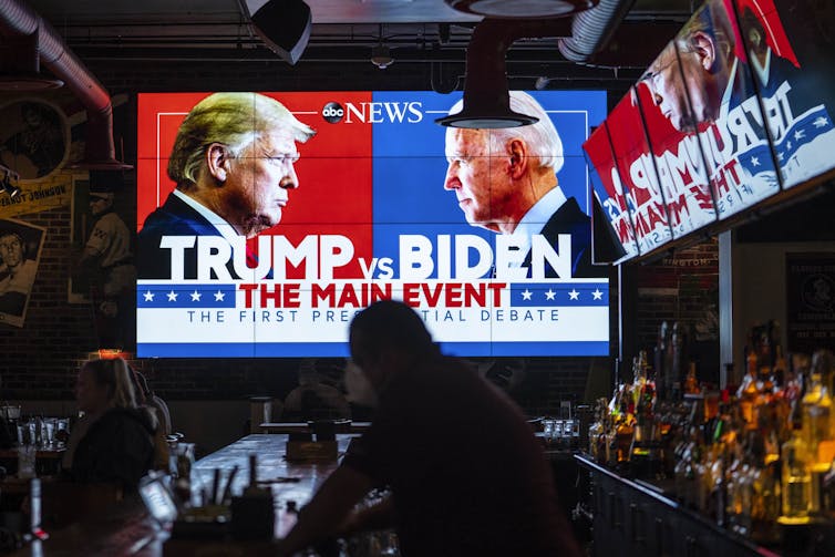 Multiple TV screens in a dark room show Trump and Biden facing each other, with the words 'Trump and Biden, the main event' on the screen.