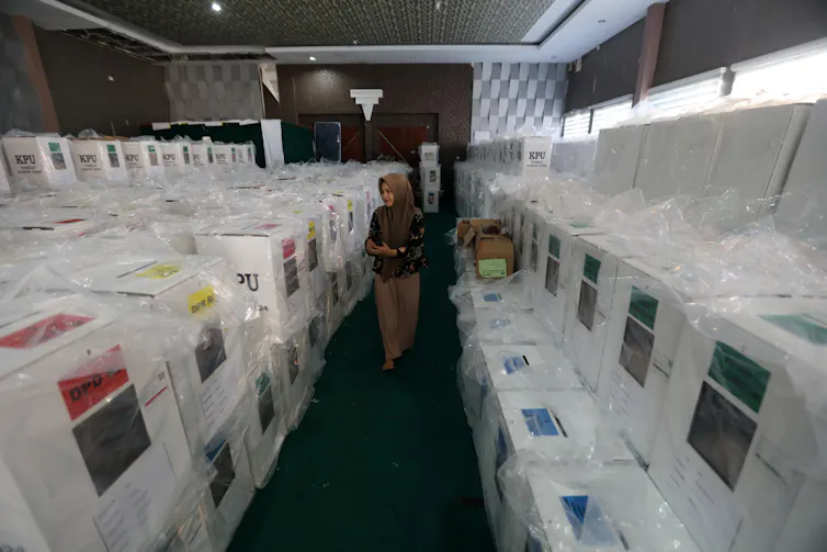 A woman in a headscarf walks among packaged polling boxes