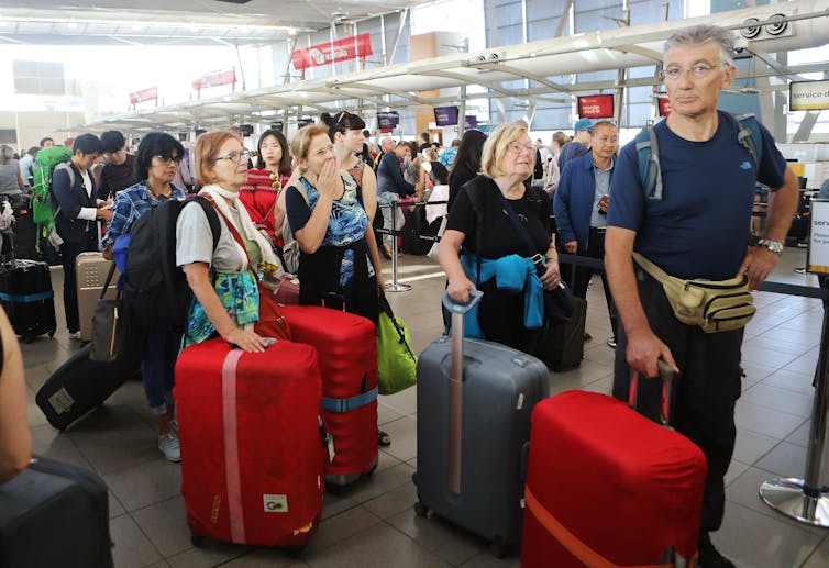 Large queue of people pushing suitcases waiting to check in at an airport
