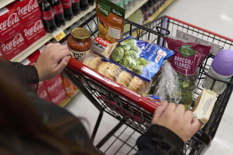Image of unidentifiable man pushing trolley full of groceries down a supermarket aisle