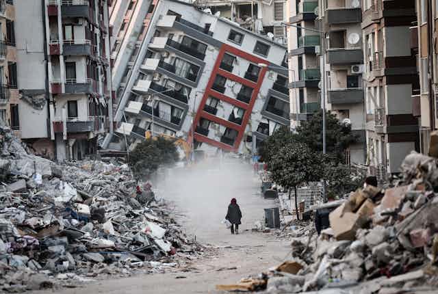 A woman walking in front of a collapsed building.