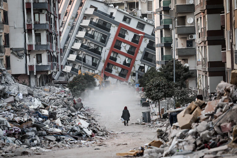 A woman walking in front of a collapsed building.