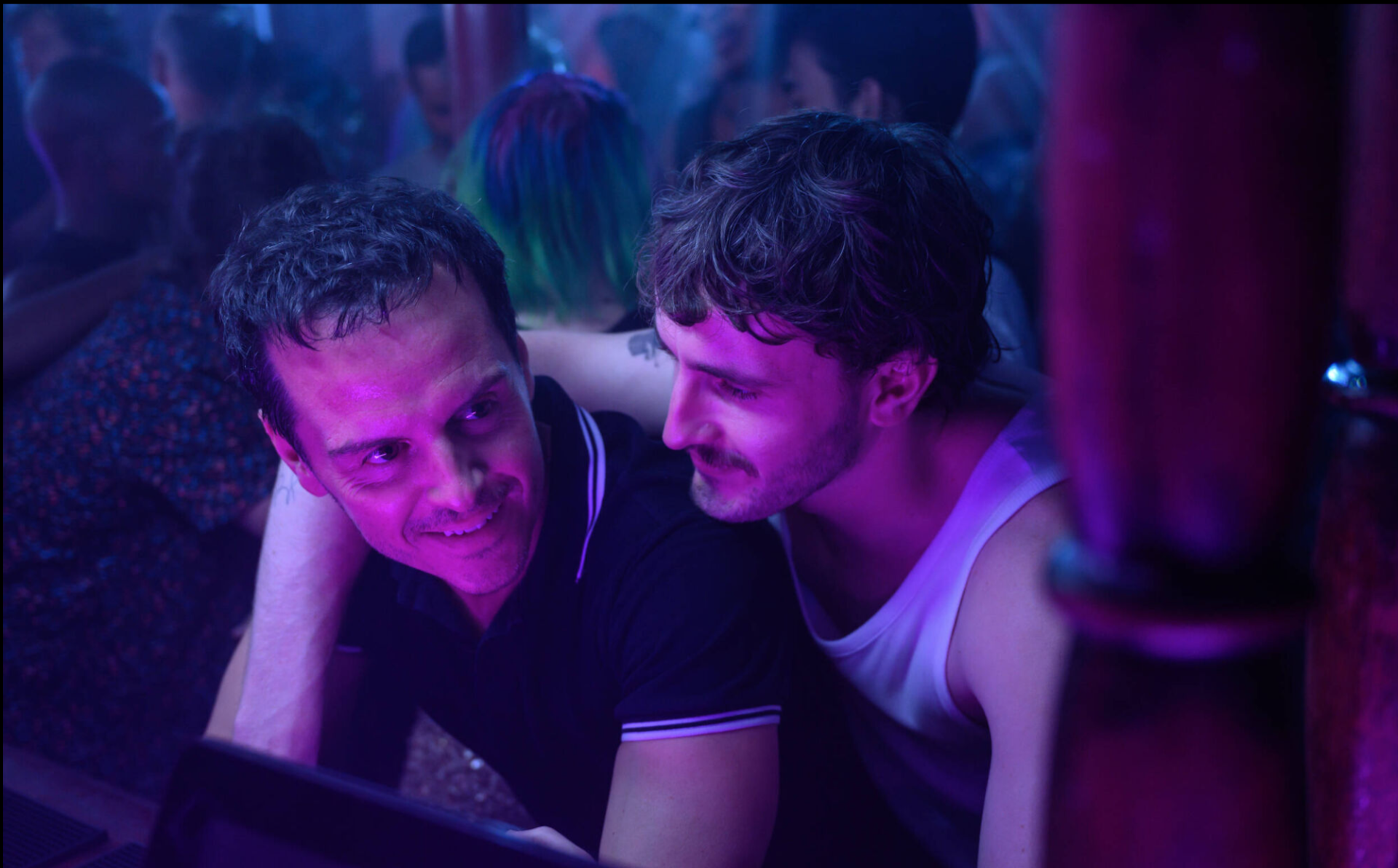 Two young gay men under the lights of a club.