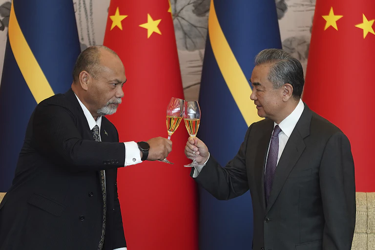 Two men standing in front of the China and Nauru flags clinking their drinks glasses together.