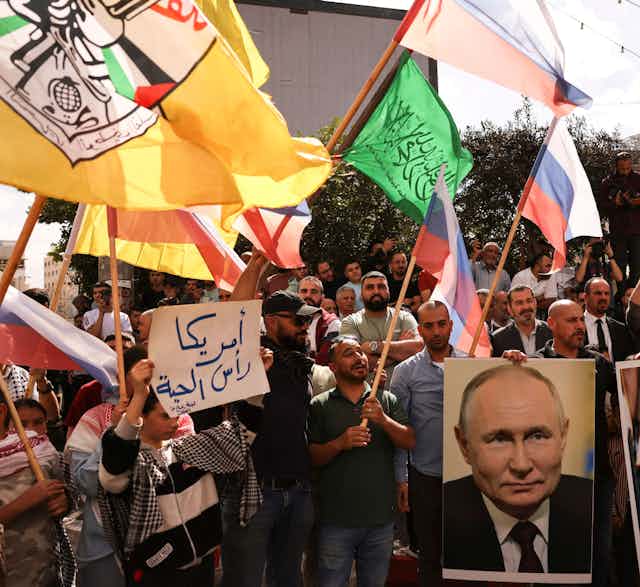 Protesters holding aloft Russian and other flags hold a poster of a man.