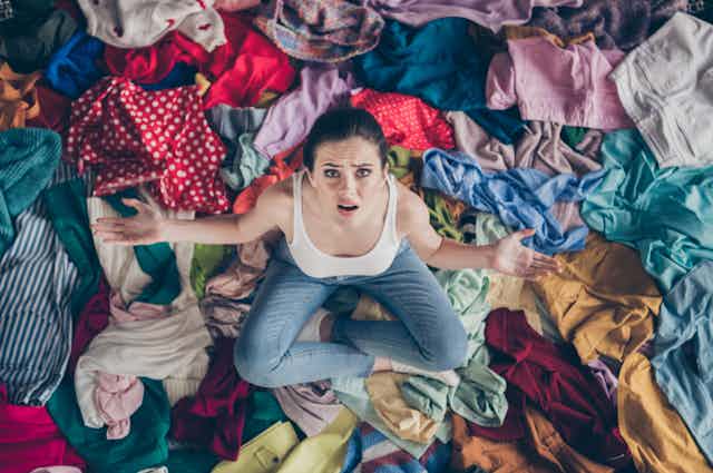 Woman with despairing look surrounded by clothes.