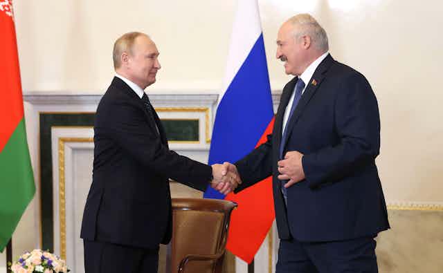 Two men in suits shake hands, Vladmir Putin and Alexander Lukashenko.