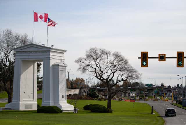 An arch with two flags seen next to a road with vehicles.