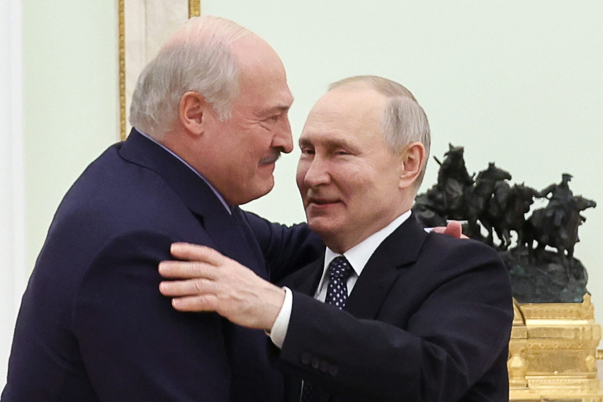 Two smiling men in suits embrace.