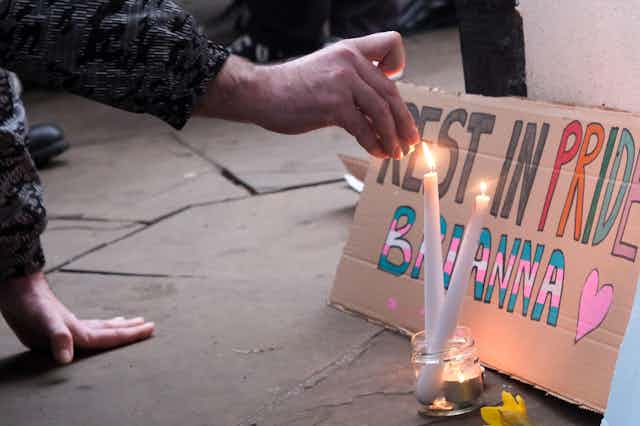 Hands lighting a candle in front of a sign saying "Rest in pride Brianna"