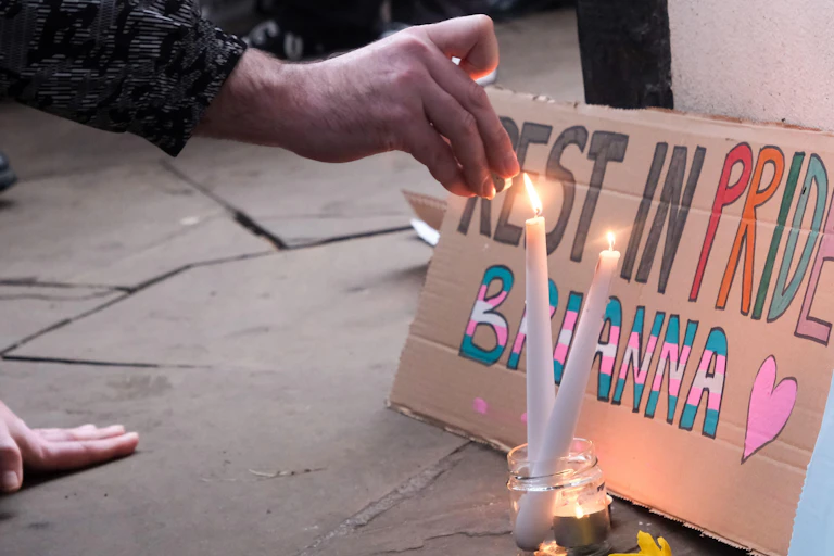 Hands lighting a candle in front of a sign saying "Rest in pride Brianna"