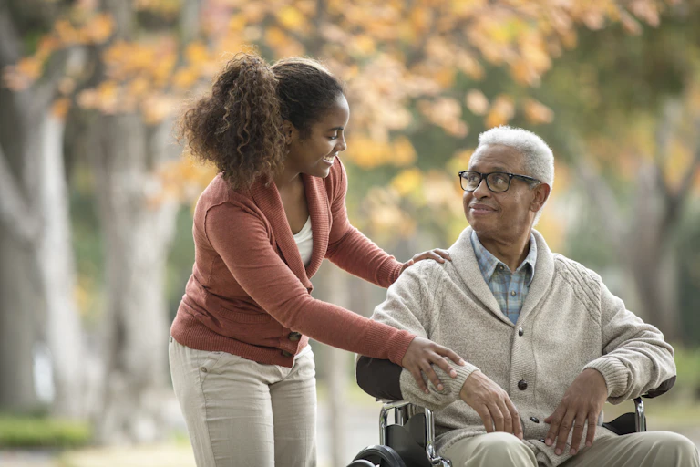 Young African American woman smiles at her father who is in a wheelchair.