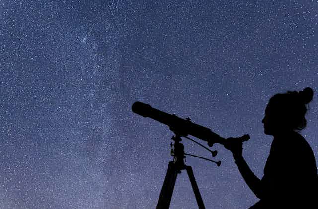 silhouette of a woman holding a telescope against a starry background