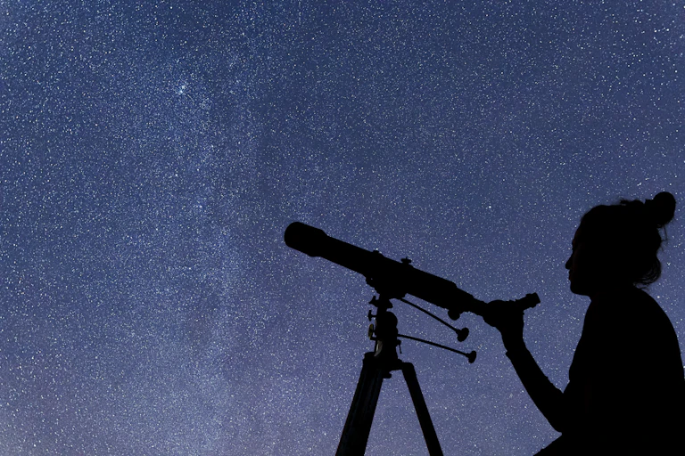 silhouette of a woman holding a telescope against a starry background