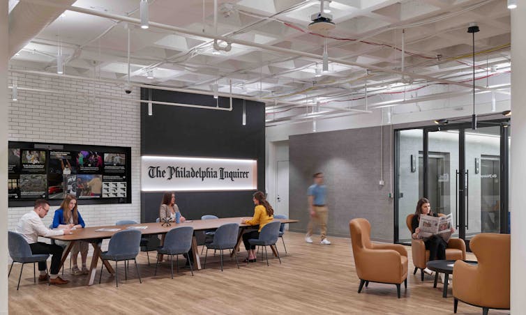 Workers sit at a table in a large, open workspace.