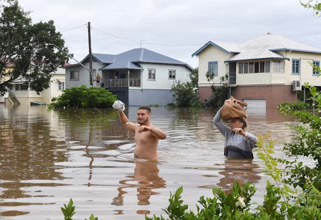 People wade through floodwaters as they evacuate their homes in Lismore