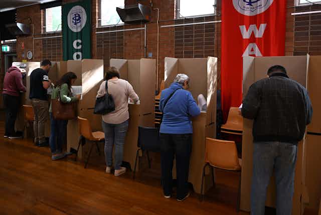 A row of people at voting booths fill out their ballot papers.