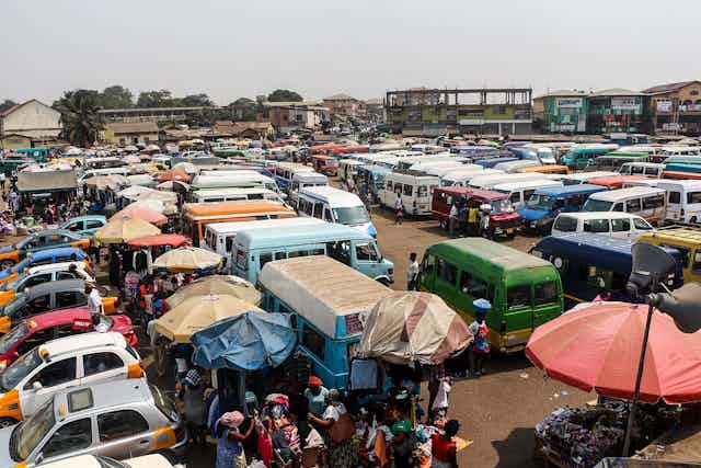 Numerous parked vehicles, with umbrellas and market stalls at the edge of the area.