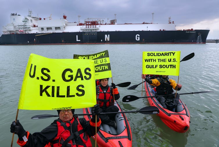 Three people in canoes hold yellow banners with messages including 'US gas kills' and an LNG tanker behind them.