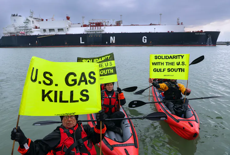 Three people in canoes hold yellow banners with messages including 'US gas kills' and an LNG tanker behind them.