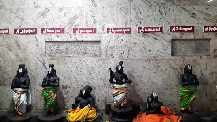 A series of icons made of black stone of male devotees, standing with folded hands, dressed in colorful, long loincloth.