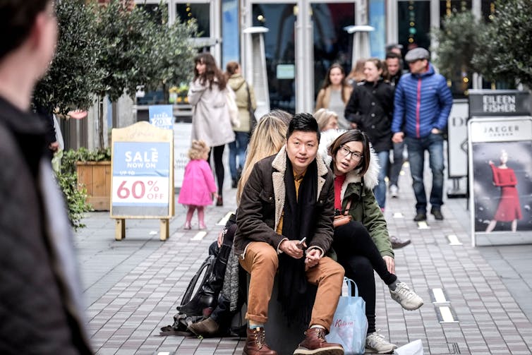 Two Chinese tourists take a rest from shopping in London, sitting down in a busy London street.