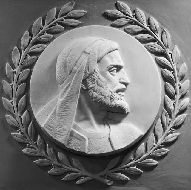 A white marble carving of a man with a beard, headscarf and a serious expression, looking off to the right.