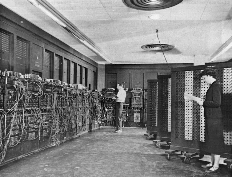 Deux personnes travaillent debout dans une grande pièce hébergeant les nombreux composants de l’ordinateur