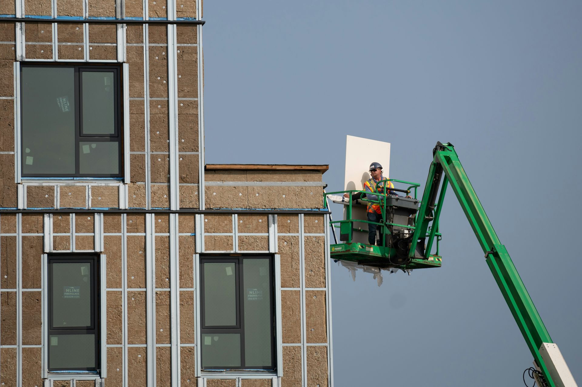 A construction worker in a boom lift move sa piece of construction equipment outside a building.