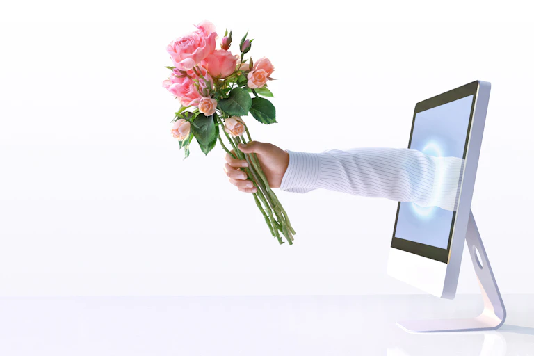 an arm reaching out from a computer screen, holding bouquet of roses