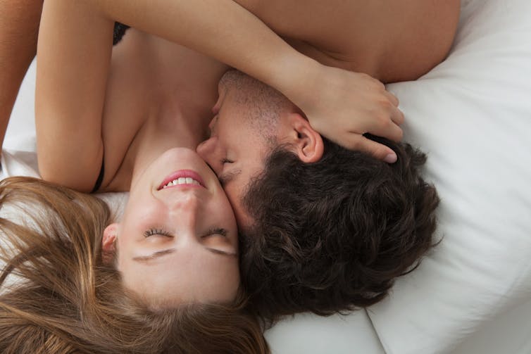 A man and woman lie in a bed hugging