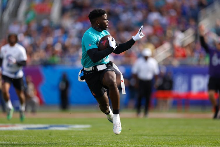 Young man runs holding a football and waving his finger mid-stride.