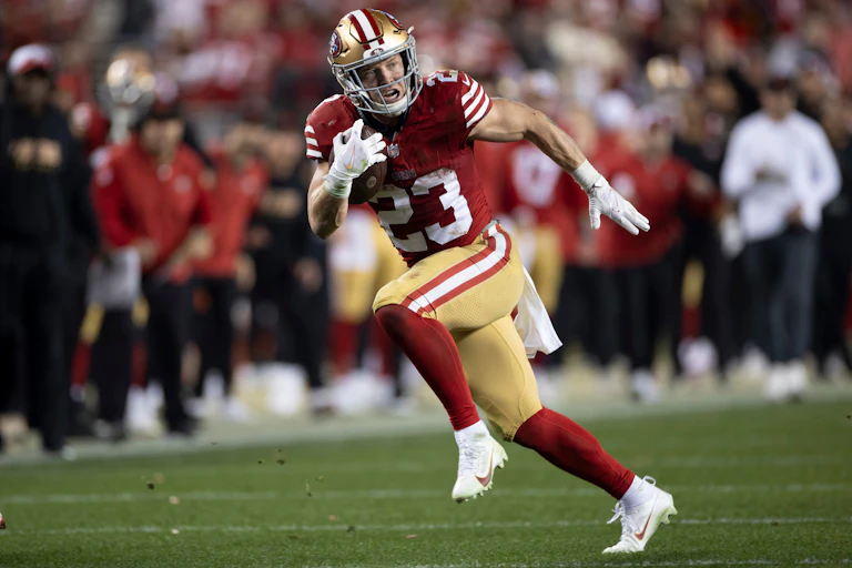 Young man wearing a football helmet and a red and gold jersey sprints while holding a football.
