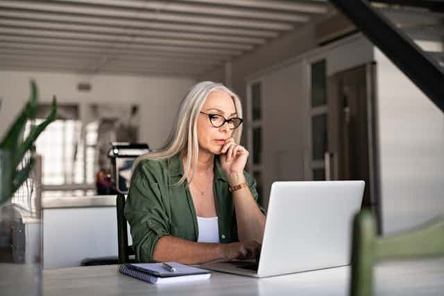 Woman with glasses looking at open laptop on desk