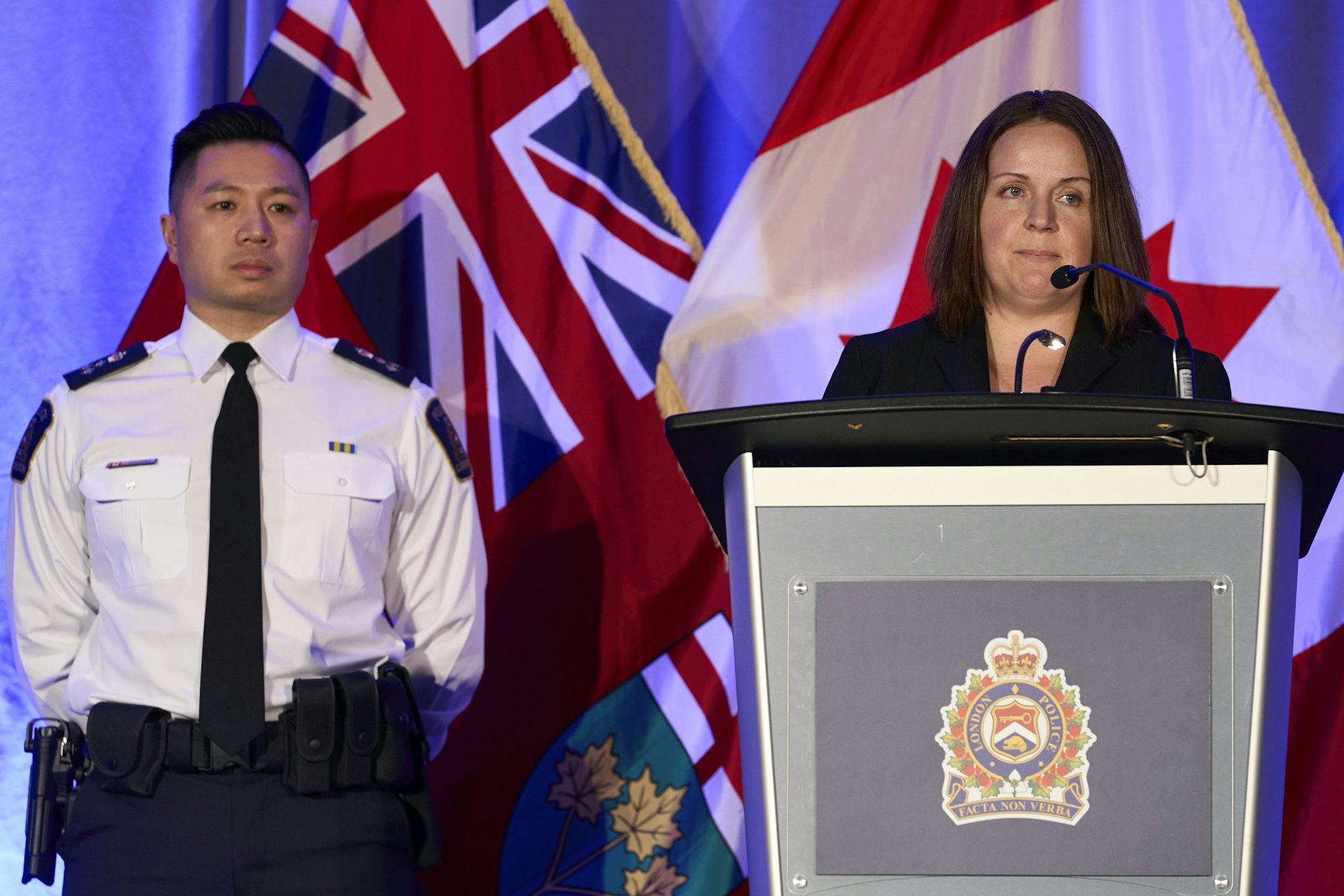 A man in a police uniform and a woman in a black blazer stand behind a lectern with the police emblem on it. In the background you can see the Canadian flag and the Ontario flag.