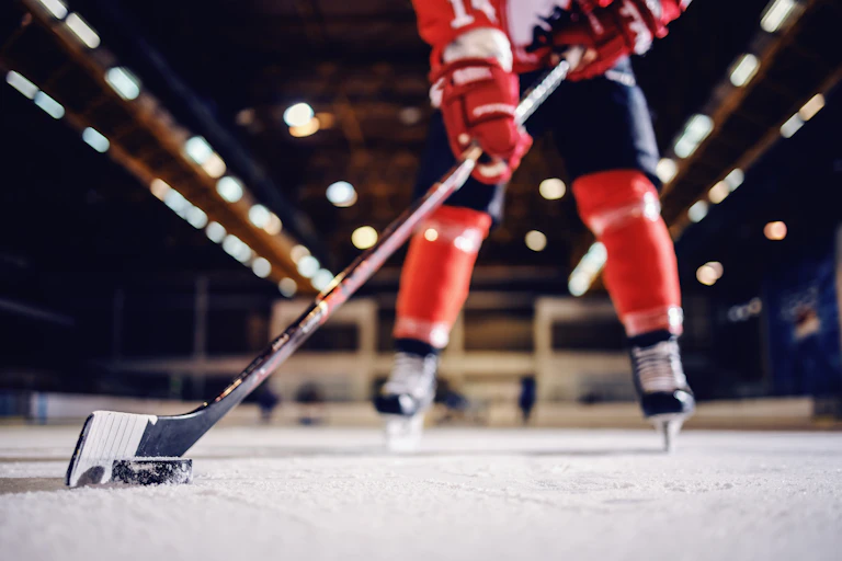 A hockey player, see from the neck down, standing on a skating rink in uniform while holding a hockey stick